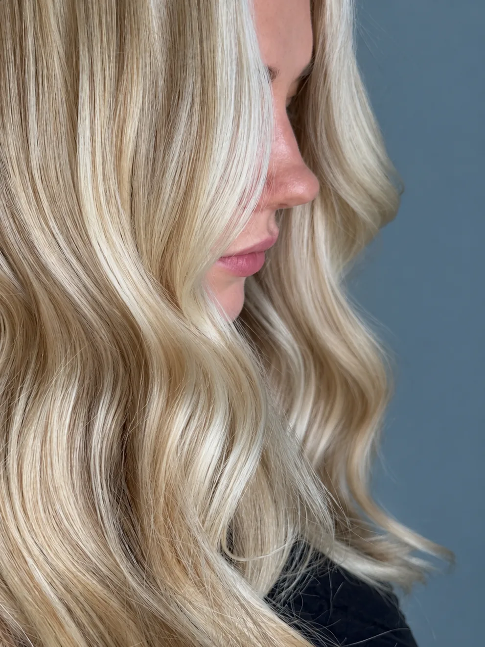 Glossy blonde hair extensions in soft waves, side profile