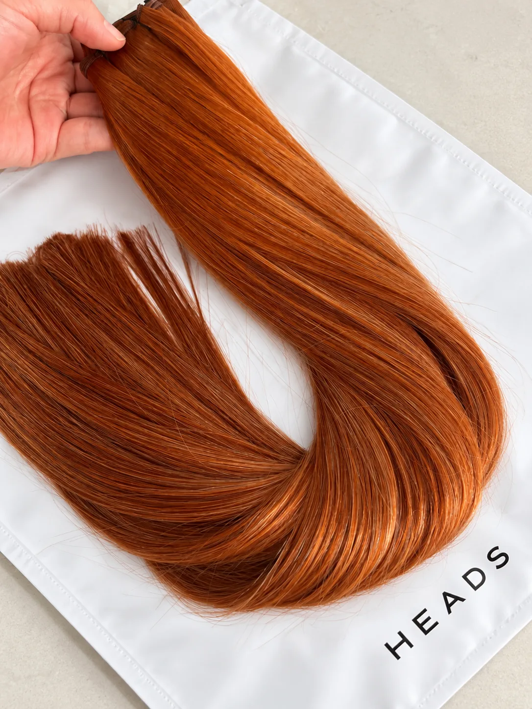 Copper weft hair extensions held over a HEADS bag
